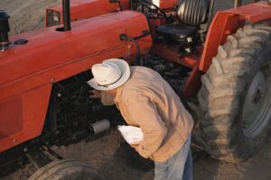 Person i cowboyhatt inspekterar motor på röd traktor utomhus
