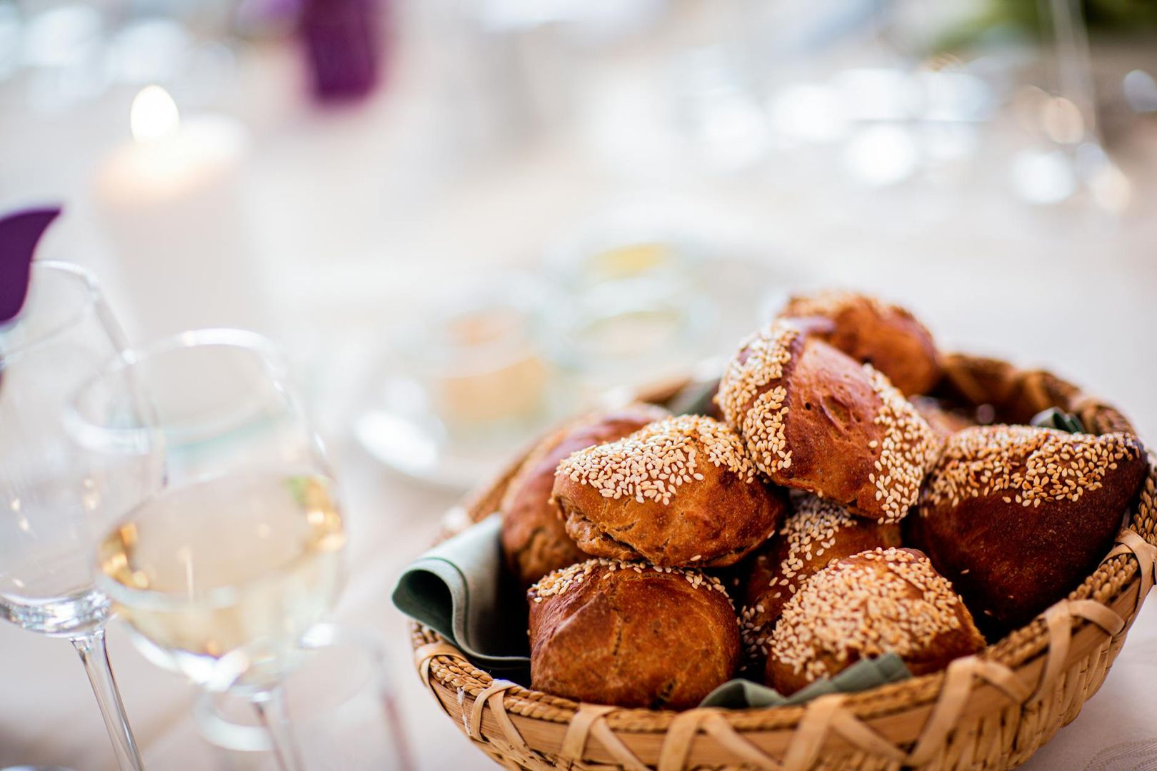 En korg fylld med färska frallor med sesamfrön på ett dukat middagsbord.